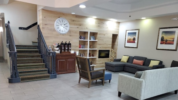 A modern living room with a staircase, a sofa set, a wooden bookshelf, and a large wall clock. - Country Inn & Suites by Radisson, Buford at Mall of Georgia, GA (Buford)