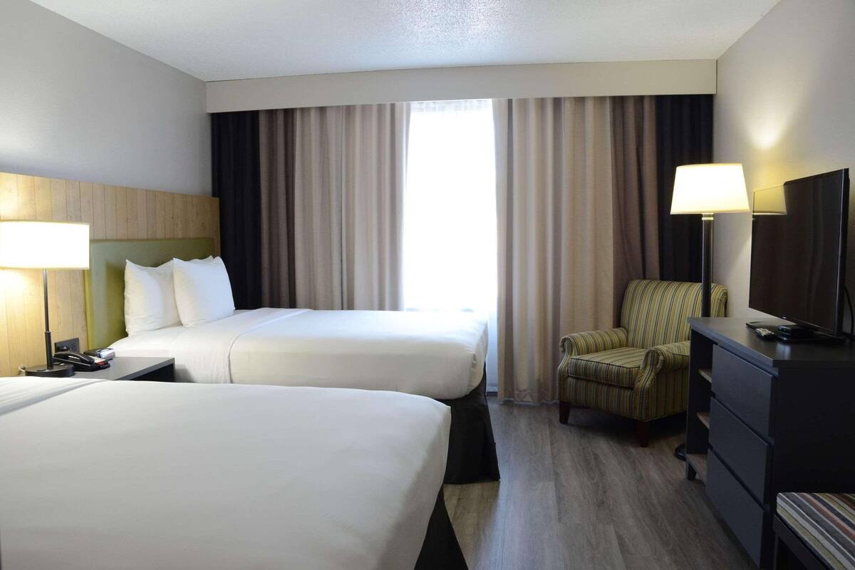 A hotel room with two beds, a chair, a TV, and a desk.
