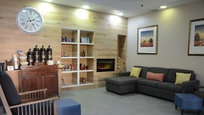 A living room with a wooden wall, a fireplace, a sofa, a coffee table, and a bookshelf. - Country Inn & Suites by Radisson, Buford at Mall of Georgia, GA (Buford)