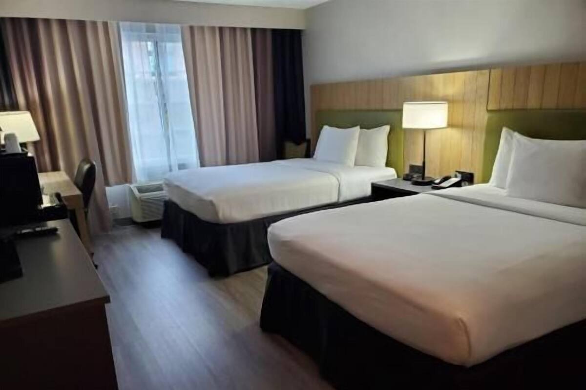 A hotel room with two beds, a desk, a chair, a lamp, and a window with curtains.