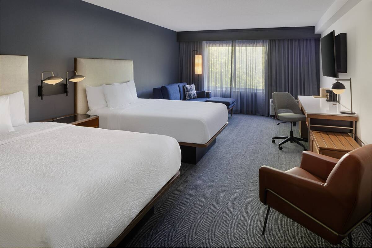 Une chambre d’hôtel avec deux lits, un bureau, une chaise et un téléviseur.