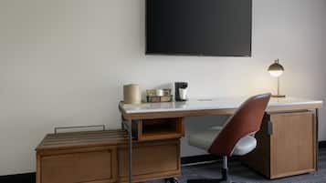 A modern office desk with a chair, a flat-screen TV, a lamp, and storage cabinets.