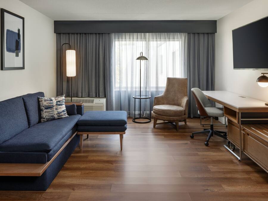 Une chambre d’hôtel moderne équipée d’un canapé, d’un fauteuil, d’un bureau et d’une télévision.