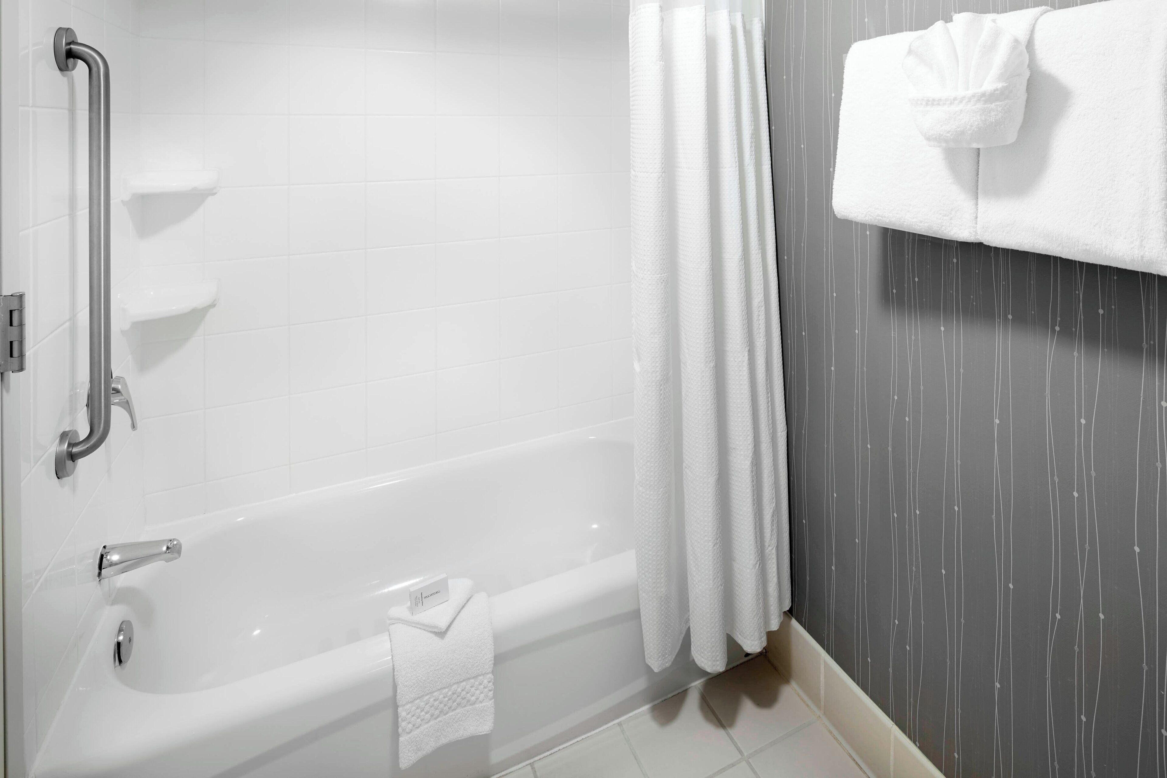 A modern bathroom with a bathtub, grab bars, and a towel rack.