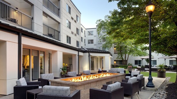 An outdoor seating area with a fire feature, wicker furniture, and a building with balconies. - Courtyard by Marriott Edison Woodbridge (Edison)