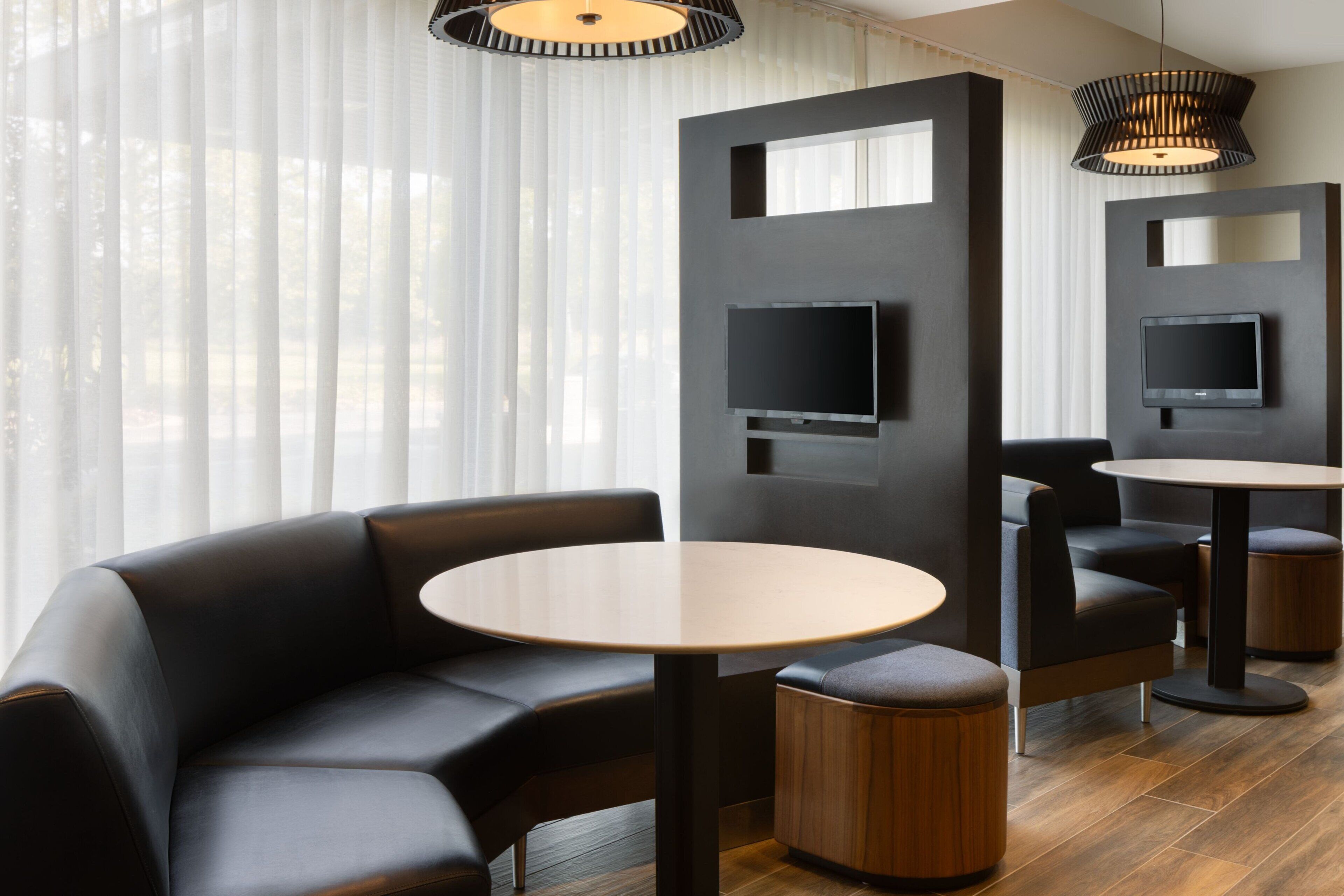 Una habitación de hotel moderna con un sofá modular, una mesa redonda y dos televisores montados en la pared.