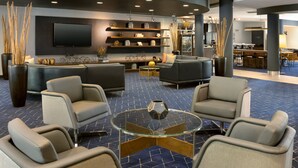 A modern lobby with a seating area, a TV mounted on the wall, and a kitchen in the background. - Courtyard by Marriott Edison Woodbridge (Edison)