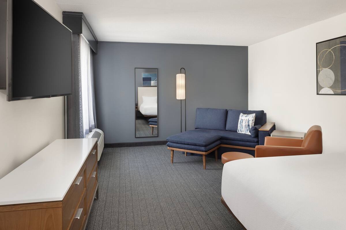 Une chambre d’hôtel avec un lit, un canapé, un bureau, un miroir et une télévision.