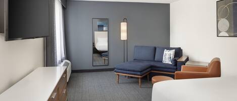 Une chambre d’hôtel avec un lit, un canapé, un bureau, un miroir et une télévision.