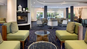 A modern lounge area with green upholstered sofas, a glass coffee table, and a fireplace. - Courtyard by Marriott Edison Woodbridge (Edison)