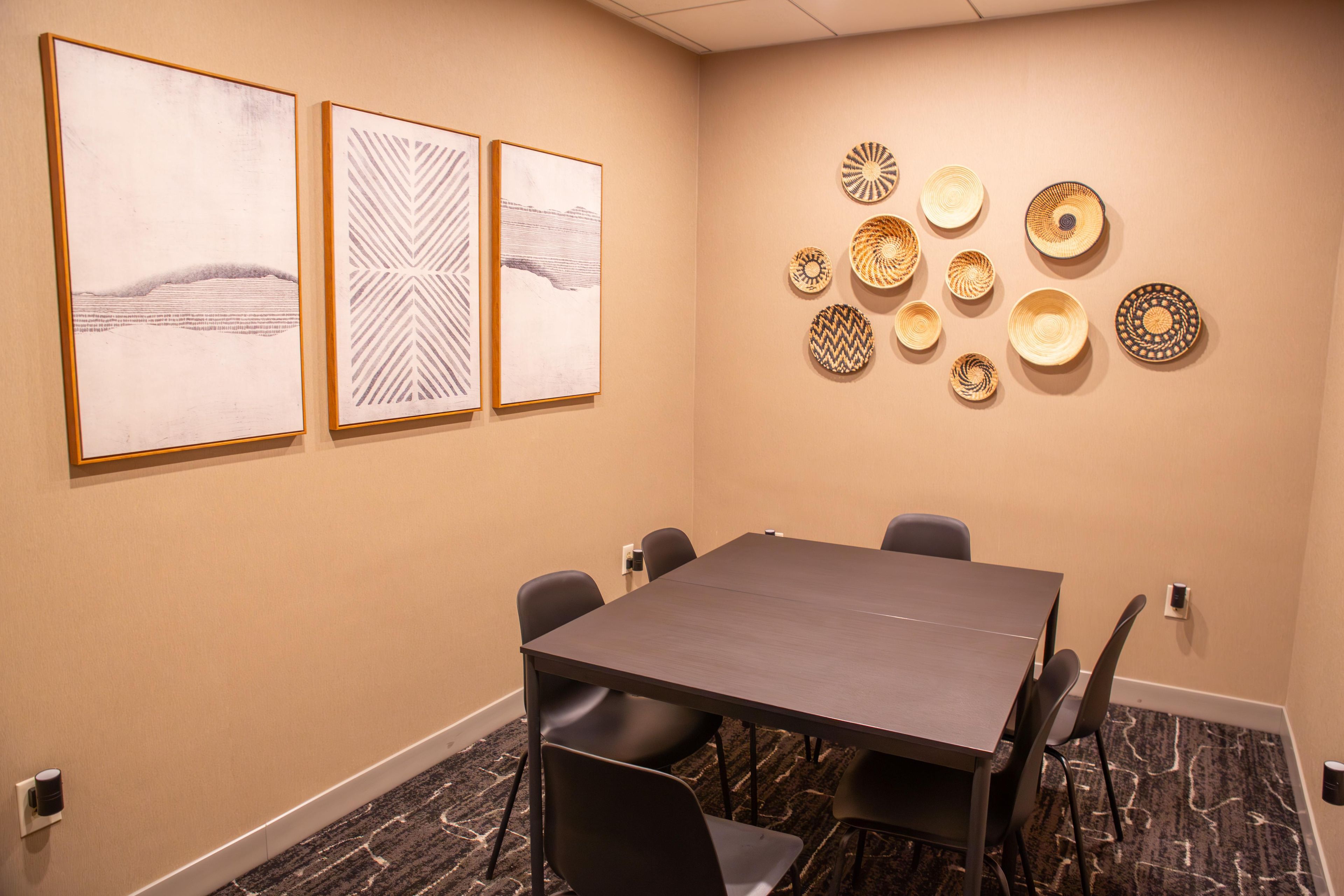 A conference room with a long table, six chairs, and three framed artworks on the wall.