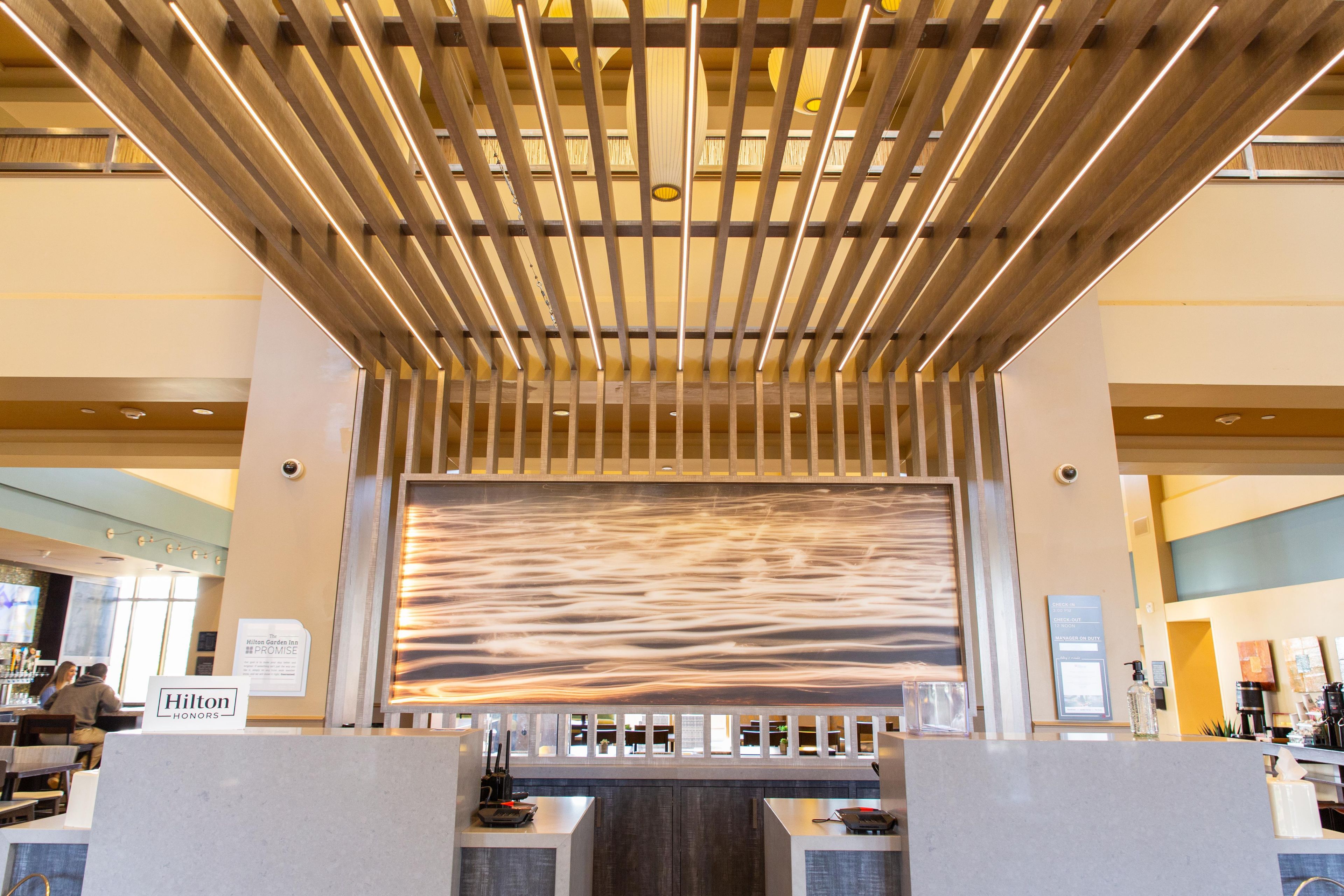 A hotel reception area with a modern design, featuring a wooden slatted ceiling and a large abstract wall art piece.