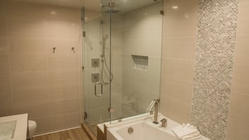 Un baño moderno con ducha envuelta en vidrio, bañera independiente y pared revestida con un diseño de mosaicos.