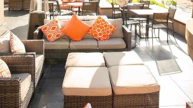 Un patio al aire libre con mobiliario de mimbre, un sofá con cojines naranja y luces colgantes.