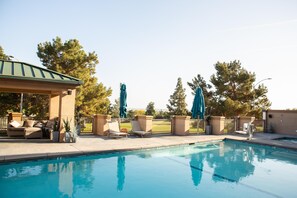 A swimming pool with lounge chairs and umbrellas, surrounded by a fence and trees. - Hilton Garden Inn Los Angeles Montebello (Montebello)