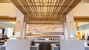 Un vestíbulo de hotel de diseño moderno, con una recepción, un gran mural abstracto y un techo con listones de madera e iluminación empotrada.