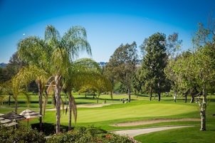Un campo de golf con búnkeres de arena, cielo despejado y varios árboles.