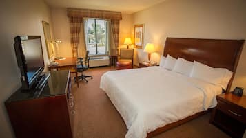 A hotel room with a bed, a desk with a computer, a chair, a lamp, and a window with curtains.