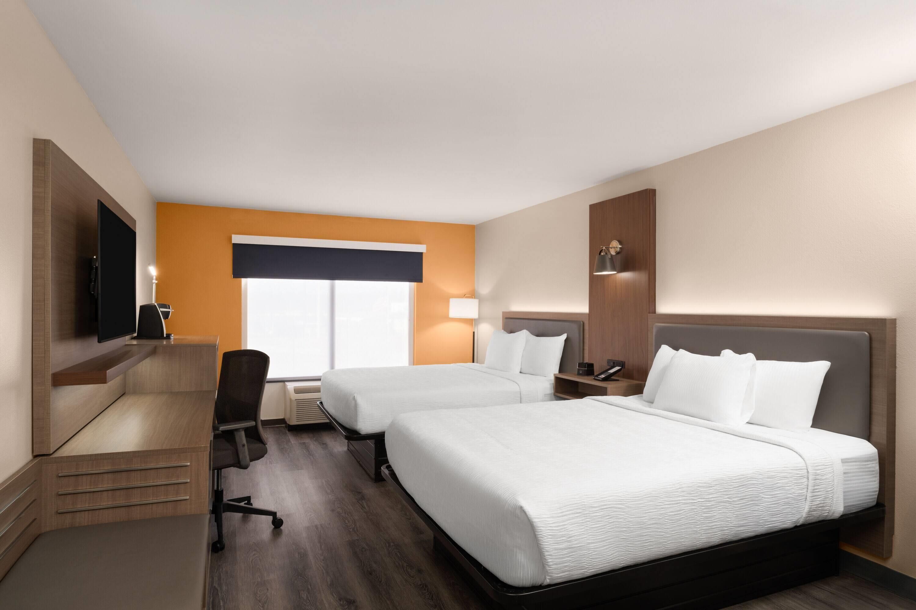 A hotel room with two beds, a desk, a chair, a television, and a window with blinds.