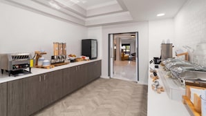A modern kitchen with a coffee machine, food dispensers, and a television. - La Quinta Inn & Suites by Wyndham Bessemer (Bessemer)