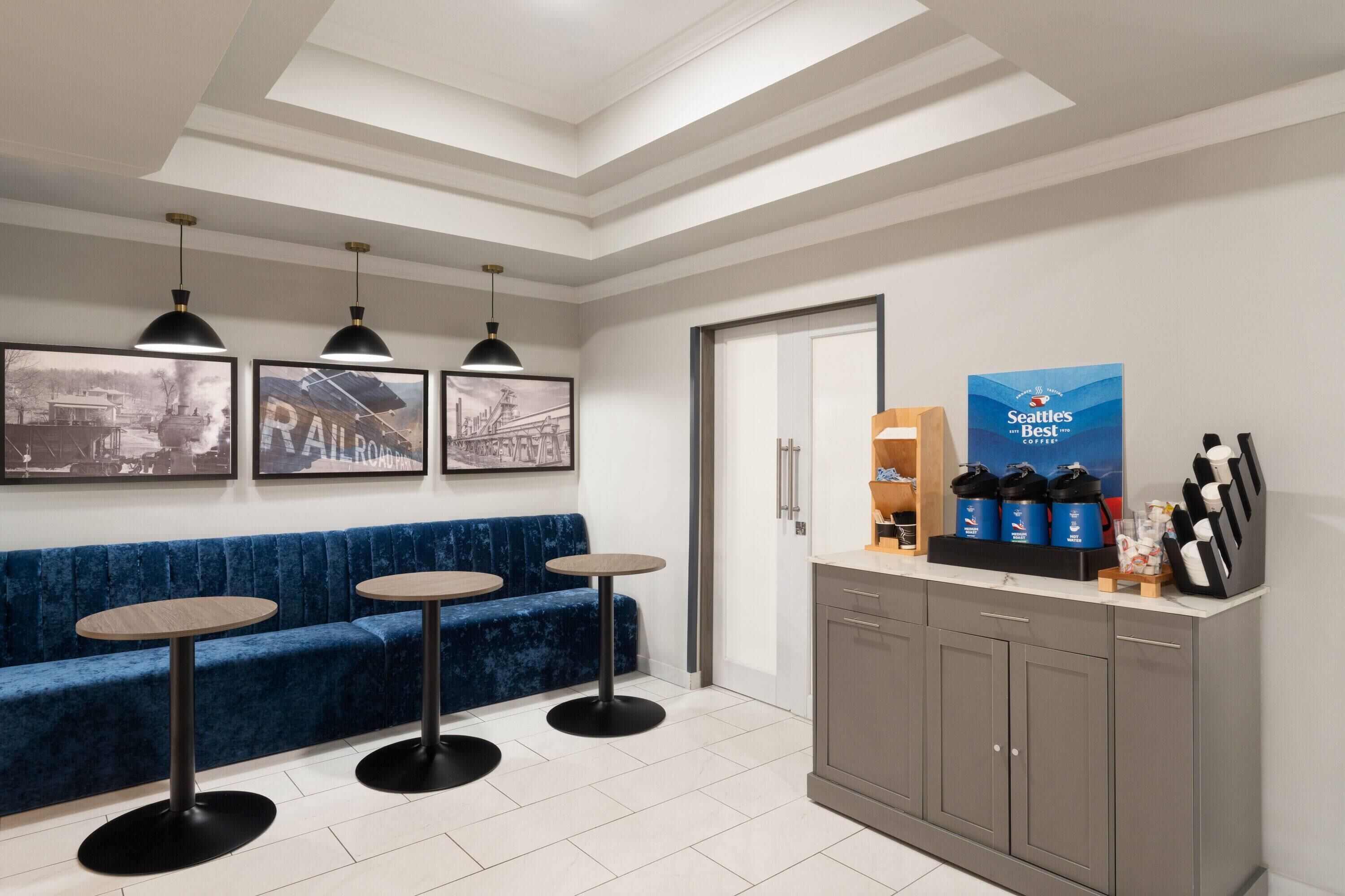 A reception area with a blue sofa, three round tables, pendant lights, a coffee station, and framed pictures on the wall.