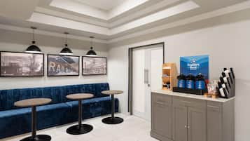 A reception area with a blue sofa, three round tables, pendant lights, a coffee station, and framed pictures on the wall.