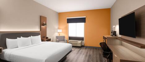 A hotel room with a large bed, a desk, a chair, a television, and a window.