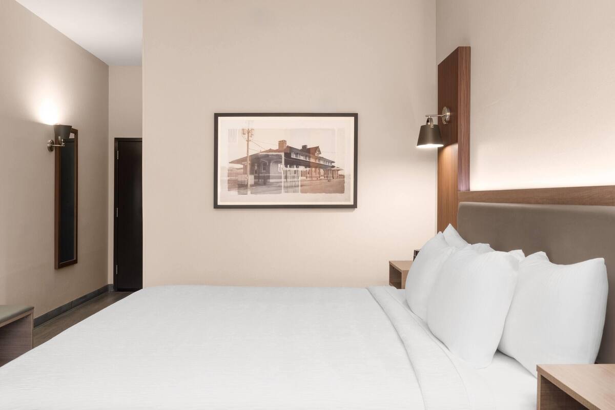 Quarto de hotel com uma cama grande, uma moldura na parede, uma mesa de cabeceira e um criado-mudo.
