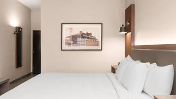 Un cuarto de hotel con una cama grande, un cuadro enmarcado en la pared, una mesita de noche y una mesita auxiliar.