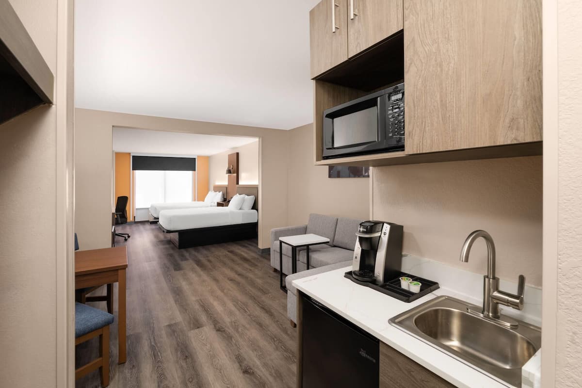 Quarto de hotel compacto com cozinha compacta, uma cama, um sofá pequeno e uma escrivaninha.