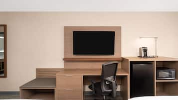Une chambre d’hôtel équipée d’un lit, d’un bureau avec une chaise, d’une télévision, d’un réfrigérateur et d’un four à micro-ondes.