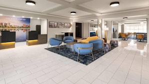 A hotel lobby with a reception desk, seating area with chairs and sofas, a coffee table, and a large poster on the wall. - La Quinta Inn & Suites by Wyndham Bessemer (Bessemer)