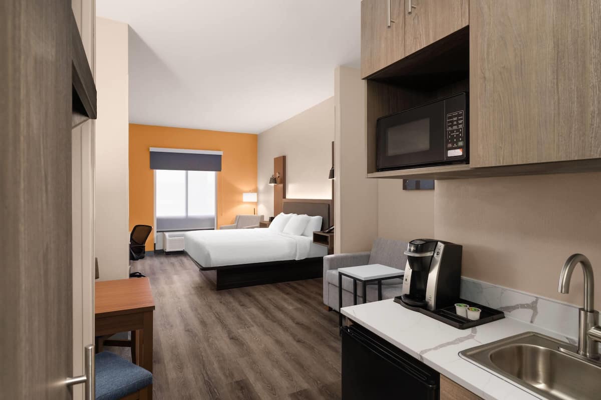 Quarto de hotel com cama, escrivaninha, micro-ondas, cafeteira e pia.