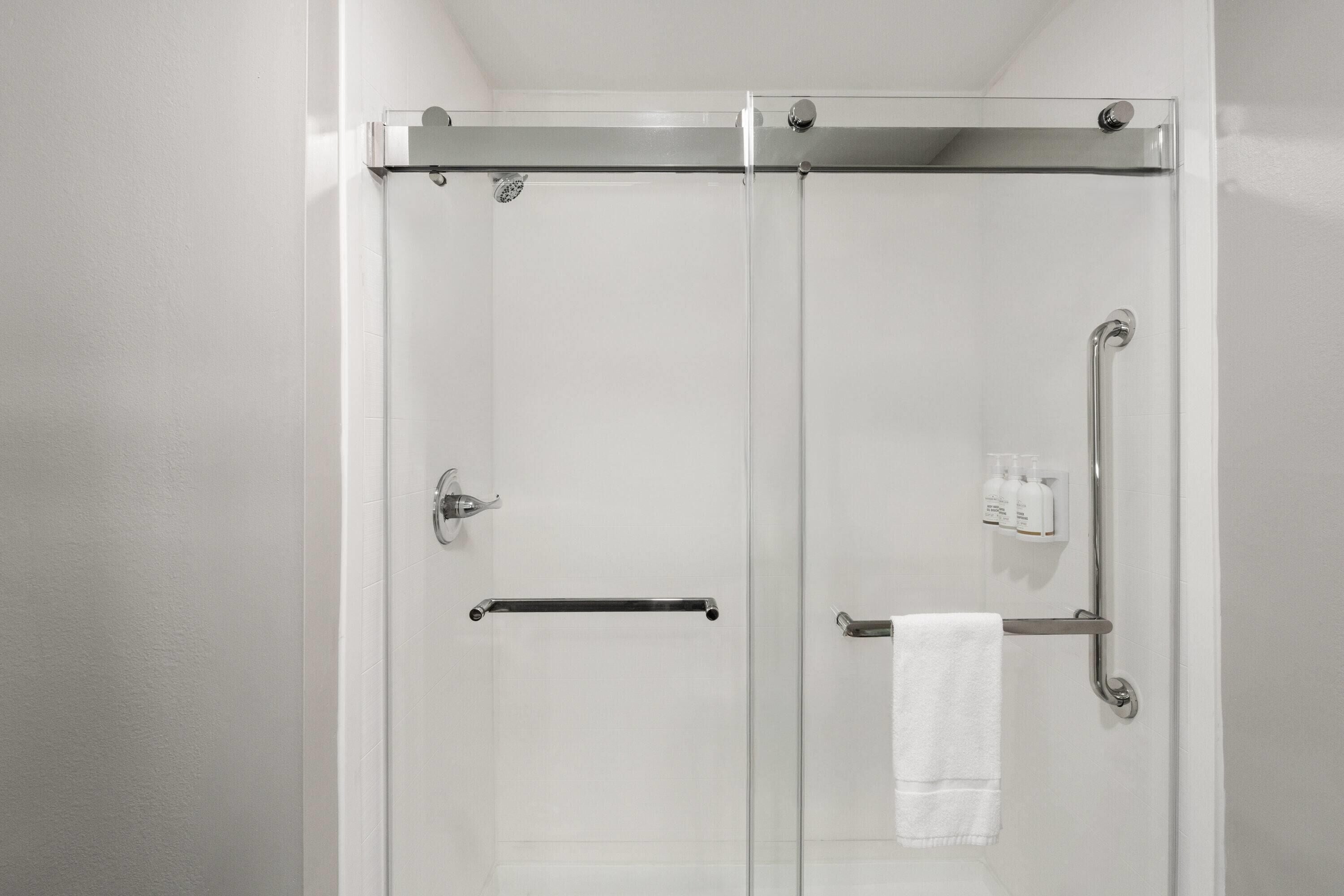 A glass-enclosed shower with a handrail, a towel rack, and a control panel.