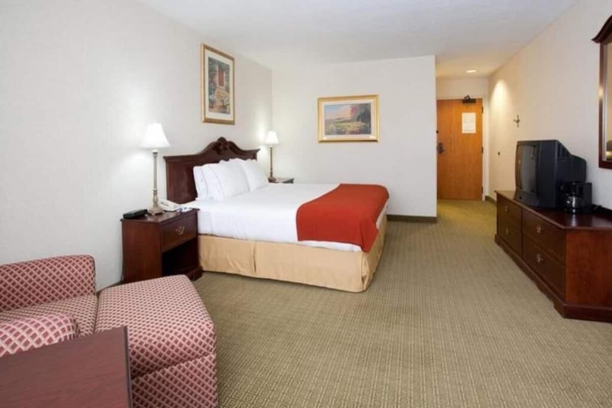 Habitación de hotel con cama, escritorio, silla, televisor y puerta.