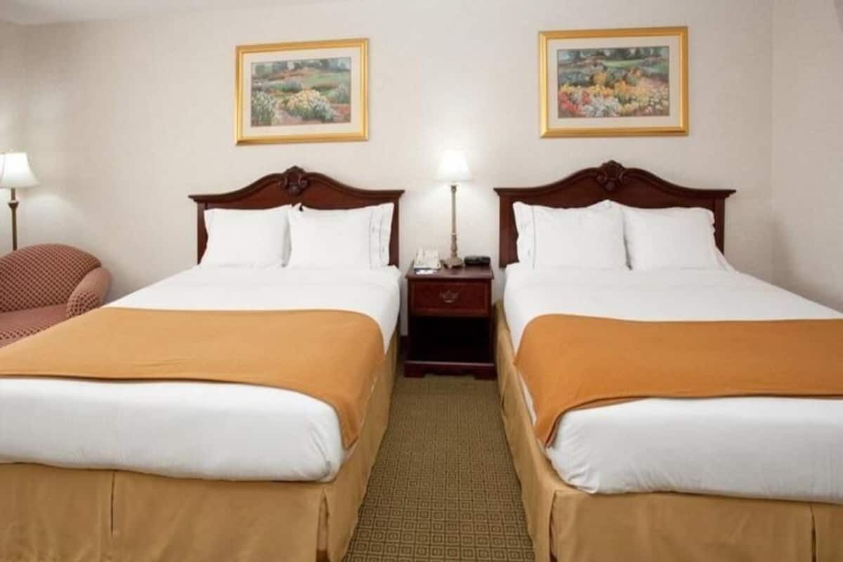 Habitación de hotel con dos camas, una mesita de noche, una lámpara y dos cuadros en la pared.
