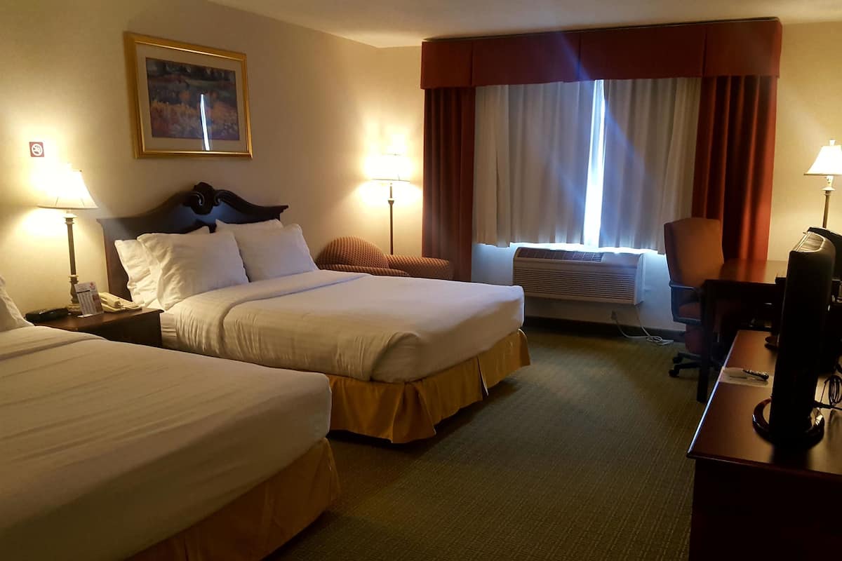 Habitación de hotel con dos camas, un escritorio, una silla, una lámpara de escritorio, un teléfono y una ventana con cortinas.