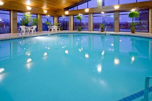 An indoor swimming pool with clear blue water, surrounded by windows and potted plants.