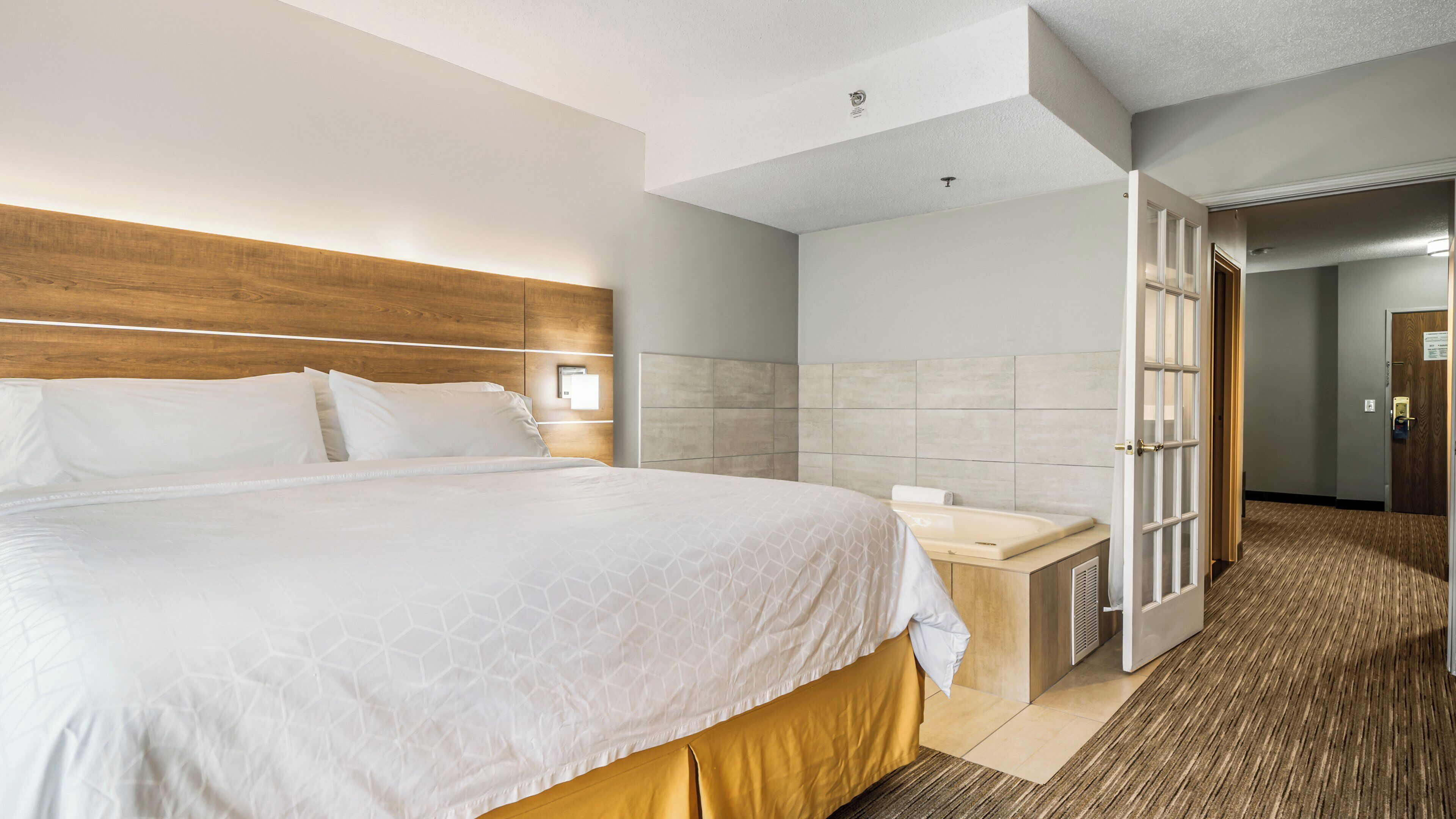A hotel room with a large bed, a bedside table, a bathroom with a shower, and a door leading to another room.