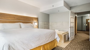 A hotel room with a large bed, a bedside table, a bathroom with a shower, and a door leading to another room. - Holiday Inn Express Hotel & Suites Bad Axe by IHG (Bad Axe)