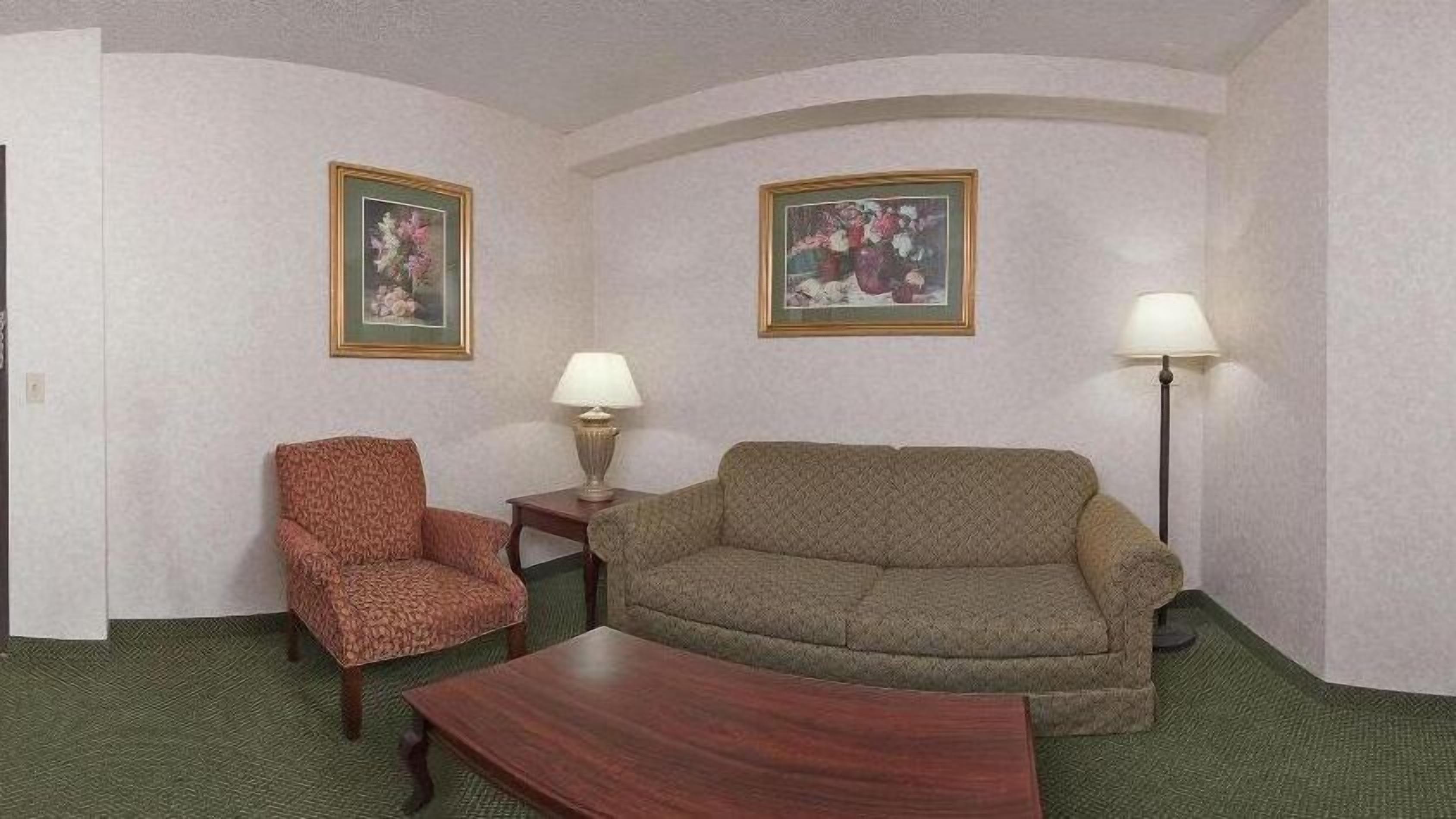 A room with a patterned armchair, a sofa, a small table, and two lamps. There are two framed floral paintings on the walls.
