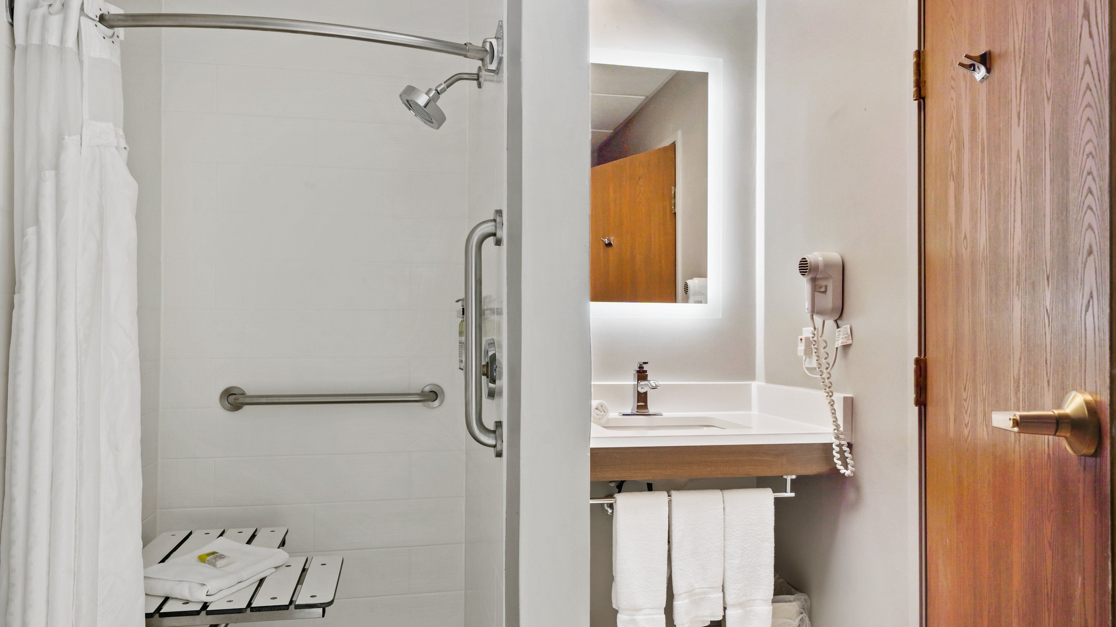 Une salle de bain équipée d’une douche, de barres d’appui, d’un lavabo, d’un miroir et d’un porte-serviettes.