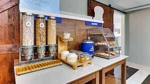 A breakfast station with cereal containers, a coffee machine, and a bakery display. - Holiday Inn Express Hotel & Suites Bad Axe by IHG (Bad Axe)