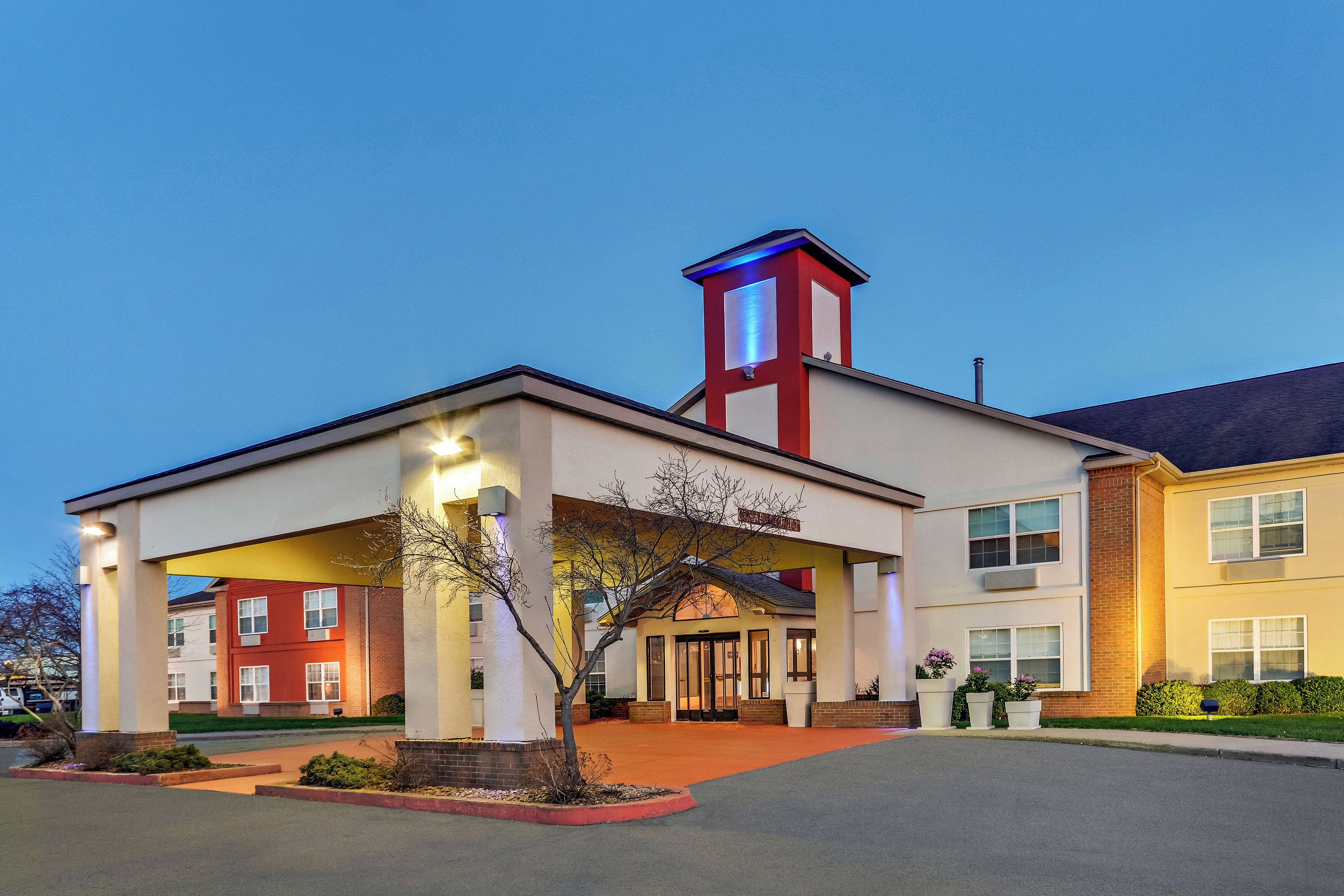 A hotel with a covered entrance, a red tower, and a parking lot.