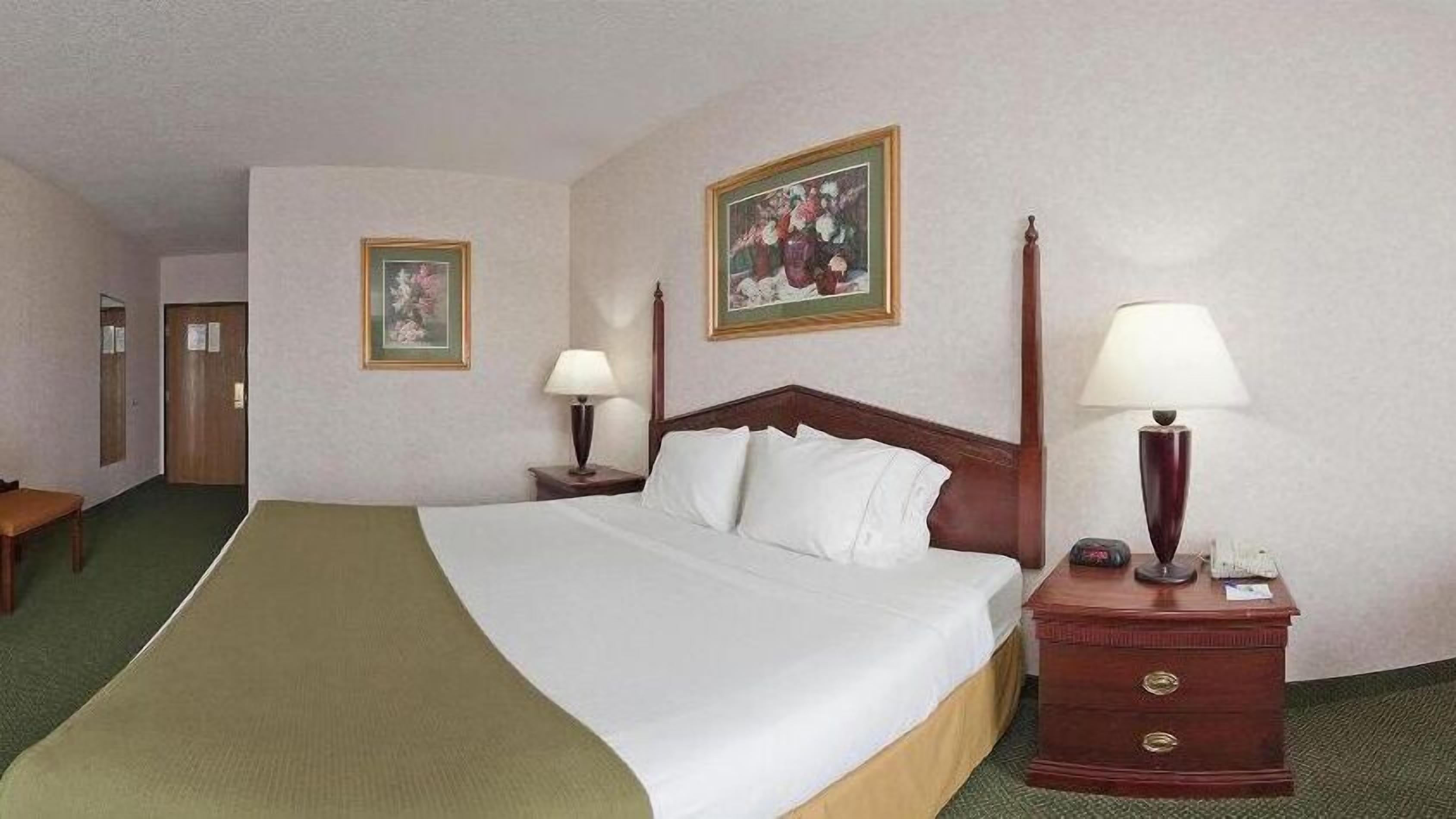 Habitación de hotel con una cama grande, dos mesitas de noche, un cabecero de madera y dos cuadros enmarcados en las paredes.