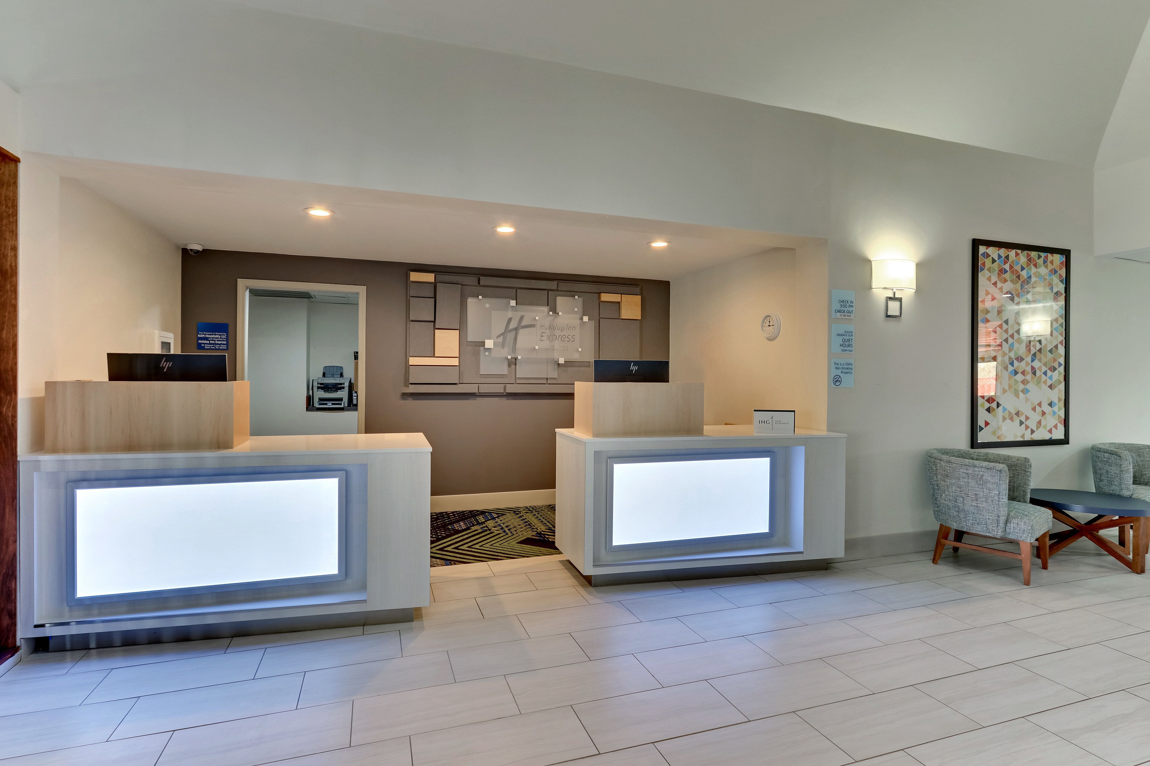 A hotel reception area with two reception desks, a clock, and a framed artwork on the wall.