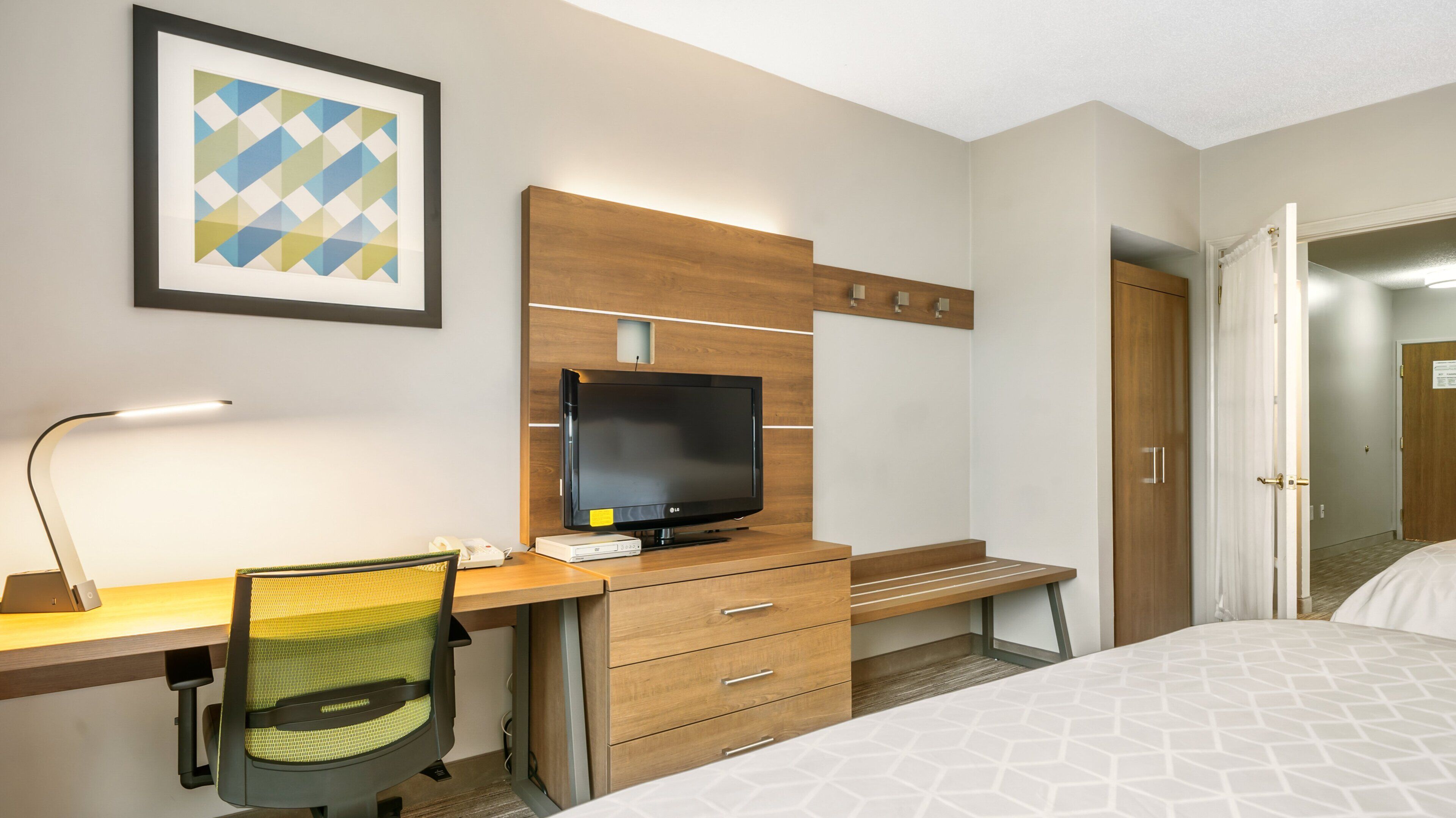 Una camera d'albergo con un letto, una scrivania con un computer, una sedia, una televisione e un armadio in legno.