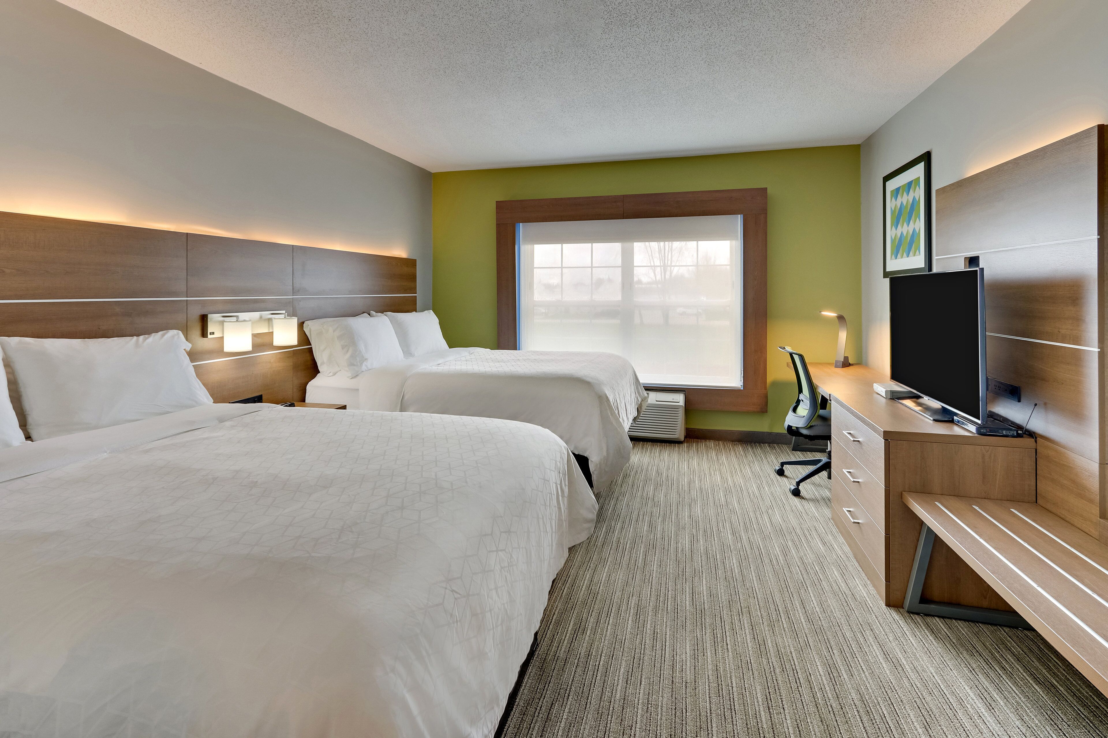 A hotel room with two beds, a desk with a computer, and a large window.