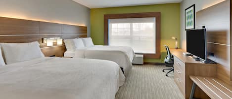 A hotel room with two beds, a desk with a computer, and a large window.