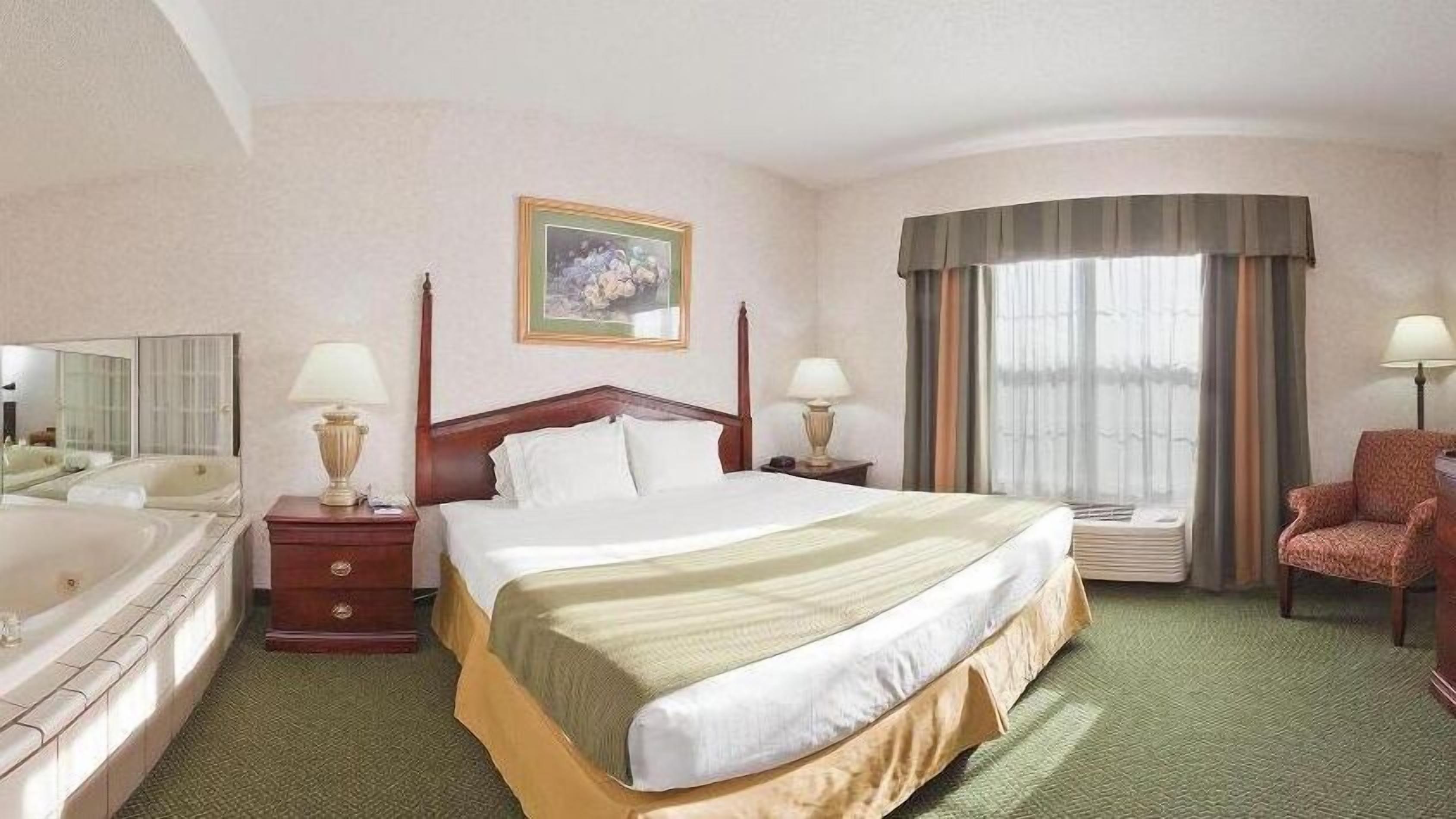 Ein Hotelzimmer mit einem großen Bett, einer Sitzecke mit einem Sessel, einer Badewanne, einem Spiegel und einem Gemälde an der Wand.